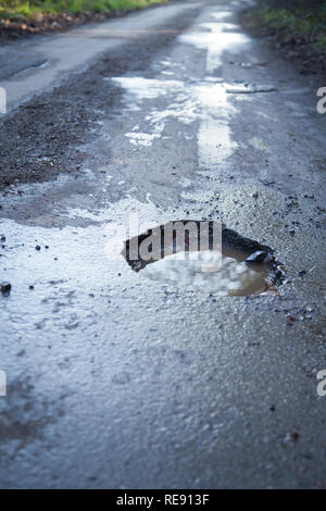 Pothole in country road in English countryside.  Asphalt road needing repair, dangerous driving surface. Stock Photo