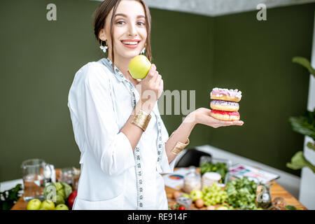 Young woman nutritionist looking on the apple choosing between healthy food and sweet dessert