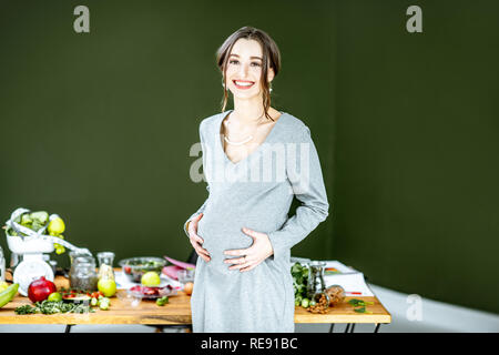 Beautiful pregnant woman with variuos of healthy food on the green background. Healthy eating and wellness during the pregnancy concept Stock Photo