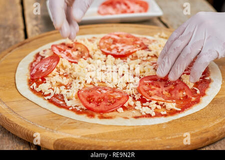 Adding tomatoes to pizza. Chef hands putting sliced tomatoes on uncooked pizza. Stock Photo