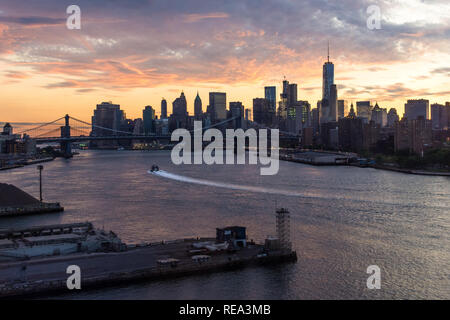 A boat crosses the East River in front of the Manhattan skyline at sunset