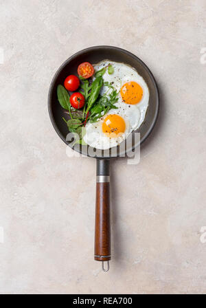 Two fried eggs on pan with fresh herbs and cherry tomatoes at light background Stock Photo