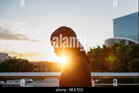 Arabic woman runner outdoors in the morning with bright sunlight. Side view of young muslim woman wearing hijab resting after workout outdoors in the Stock Photo