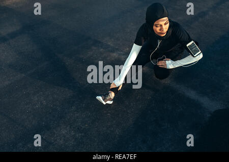 Healthy muslim woman with hijab doing exercise in morning. Hijab girl doing leg stretching workout on the street. Stock Photo