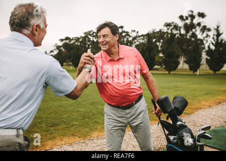 Cheerful senior golfers hand shake at driving range. Two mature golf players shaking hands after a successful practise session at driving range. Stock Photo