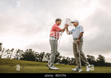 Two senior friends shaking hands at golf course after the game. Professional golfers enjoying the game on field. Stock Photo