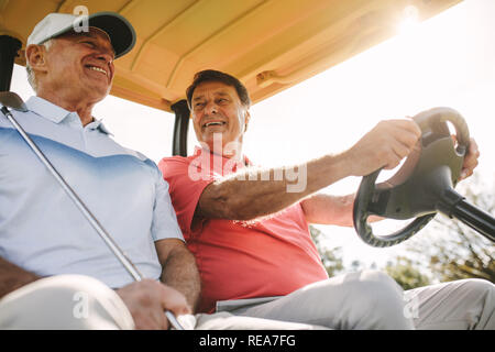 Low angle shot of two senior men driving in a golf cart. Two male golfers in a cart enjoying a round of golf on a sunny day. Stock Photo