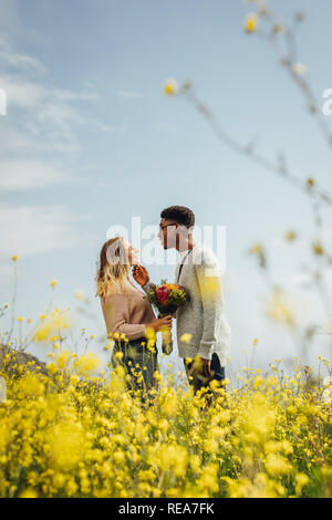 Side view of young man looking at his girlfriend holding flowers outdoors. Interracial couple standing together and looking at each other with love. Stock Photo