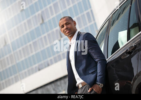 Young man standing near car hand in pocket looking camera thoughtful bottom view Stock Photo