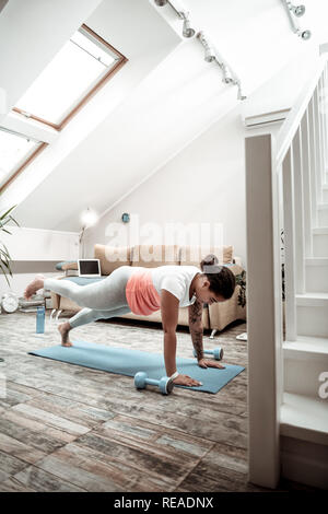 Curly dark-skinned lady doing sport in her duplex apartment Stock Photo