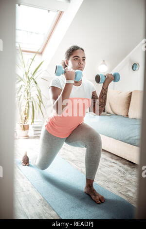 Resolute African American woman raising hand burdened with heavy dumbbells