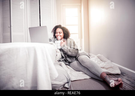 Cheerful African American lady sitting on blanket in her bedroom Stock Photo