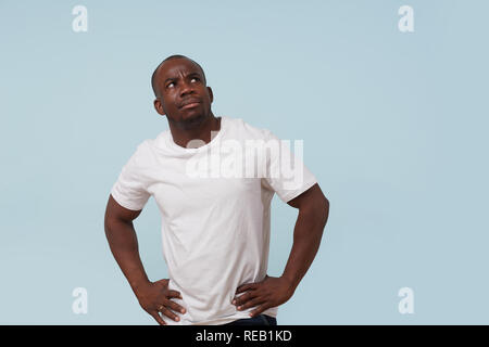 Handsome serious bold black man in white T-shirt with hands on waist, against pale blue background. Displeased, grumpy, unsatisfied, upset, angry. Stock Photo
