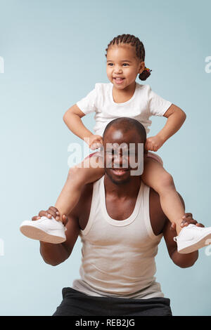 Handsome black young father is doing squats with his cute little daughter riding him. He is having trouble with additional weight, which is funny to h Stock Photo