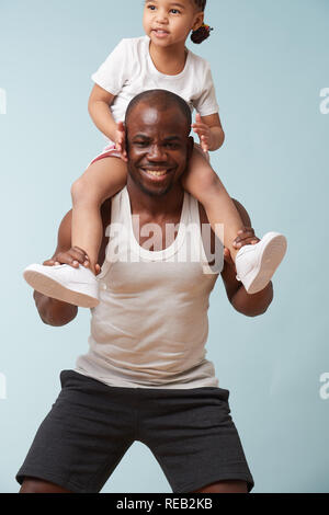 Handsome black young father is doing squats with his cute little daughter riding him. They have fun, laugh together. Stock Photo