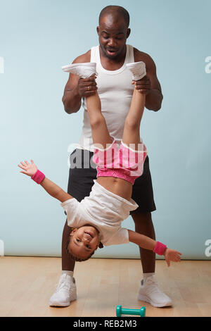 Handsome black young father is holding his cute little daughter upside down at home. She enjoys it big time, swinging from side to side. Stock Photo