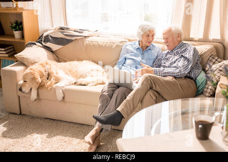 High angle portrait of modern senior couple using digital tablet sitting on couch at home in sunlight copy space Stock Photo