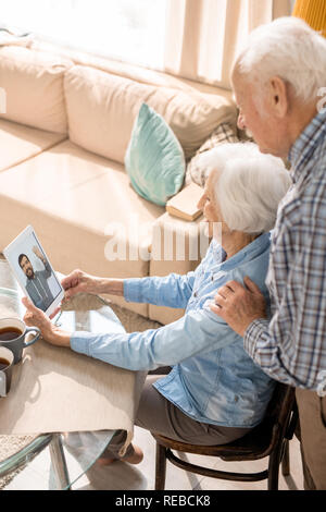 High angle portrait of modern senior couple using digital tablet and smiling while video chatting with son at home Stock Photo