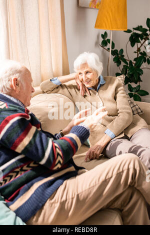 Portrait of cute senior couple talking sitting on sofa at home Stock Photo