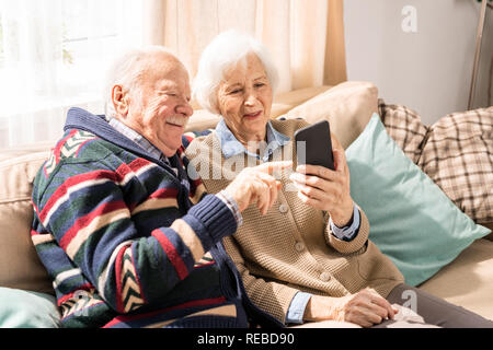 Portrait of adorable senior couple using smartphone together video chatting with family at home, copy space Stock Photo