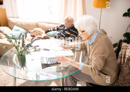 Warm toned side view portrait of senior woman filling tax forms at home, copy space Stock Photo