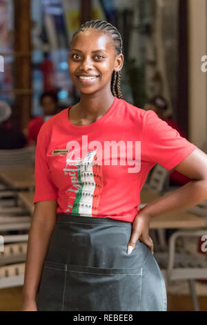 Durban, South Africa - January 06th, 2019: Portrait of a black waitress south african woman with braids smiling looking camera in Durban Stock Photo