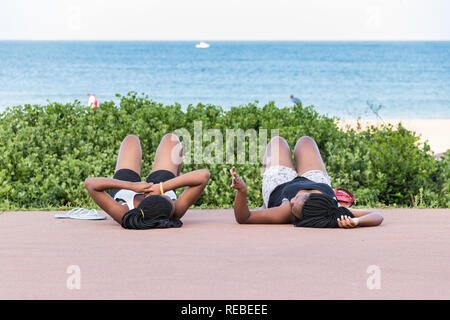 Durban, South Africa - January 06th, 2019: Two black south african womenwith braids lying down in the beach, talking in Durban, South Africa. Stock Photo