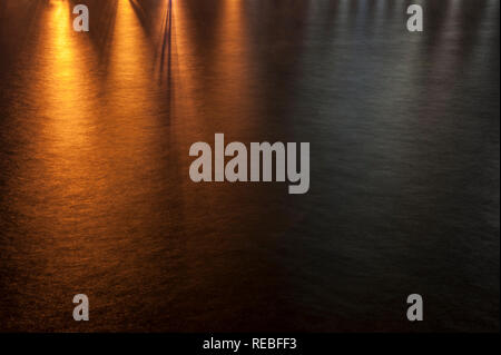 Orange tungsten light reflecting off of moving water in the bay Stock Photo