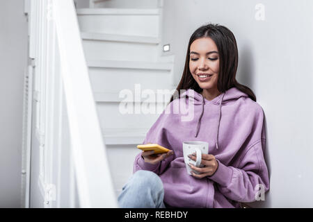 Stylish young woman feeling relaxed drinking tea sitting on stairs Stock Photo