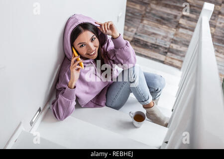 Dark-haired woman wearing jeans and purple hoodie calling her friend Stock Photo