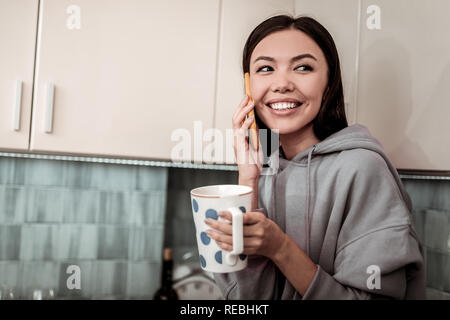 Cheerful woman feeling good drinking tea and speaking on phone Stock Photo