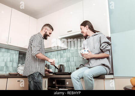 Bearded man feeling joyful while making dinner for wife Stock Photo