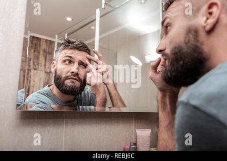 Bearded dark-haired man looking at acne on his face Stock Photo