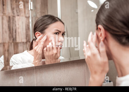 Dark-eyed young woman seeing pimples on her face Stock Photo