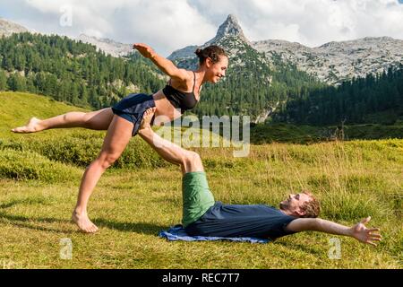 Young woman and young man doing acro yoga, mountain landscape, Berchtesgaden National Park, Berchtesgadener Land, Upper Bavaria Stock Photo