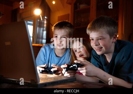 Siblings, 7, 11, 13 years old, with laptop computer in the living room, playing a car racing computer game Stock Photo