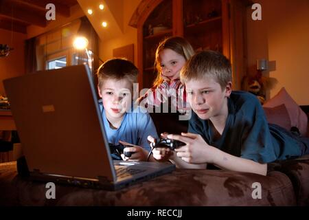 Siblings, 7, 11, 13 years old, with laptop computer in the living room, playing a car racing computer game Stock Photo