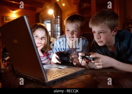 Siblings, 7, 11, 13 years old, with laptop computer in the living room, playing a car racing computer game