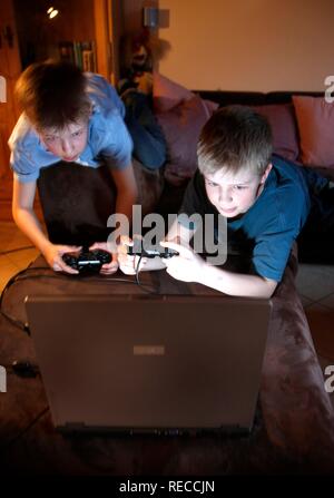 Brothers, 11 and 13 years old, with laptop computer in the living room, playing a car racing computer game Stock Photo