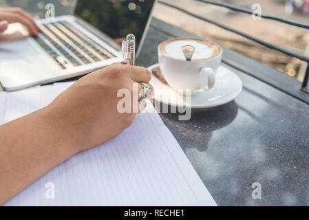 Businessman typing laptop by left hand, writing note by right hand Stock Photo