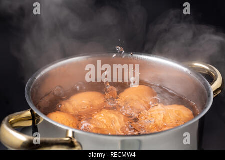 cooking brown chicken eggs in boiling steaming water on electric stove, closeup, front view, black background Stock Photo