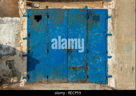 Rusty blue metal garage door in a weatherbeaten stone wall Stock Photo