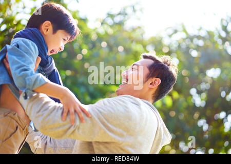 asian father having fun lifting son oudoors in park. Stock Photo