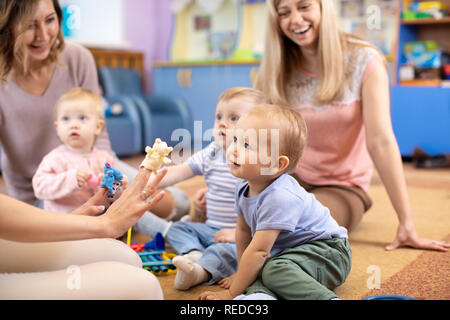 Nursery teacher and babies playing with educational toys in kindergarten or day care centre Stock Photo