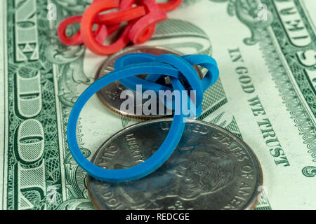 Twisted red blue rubber bands and coins on dollar bills in a close up view conceptual of trade, business, investment, savings, retirement, finance and Stock Photo