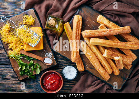 Cheese Straws, Cheesy BreadSticks on a cutting wooden board with grated cheddar cheese, tomato sauce, olive oil on a table, view from above, close-up, Stock Photo