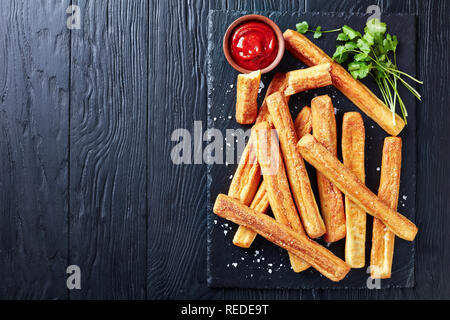 Cheese Straws, Cheesy Bread Sticks on a cutting wooden board with tomato sauce on a black wooden table, view from above, close-up, flatlay, copy space Stock Photo