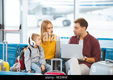 surprised kid in headphones looking at dad while sitting near mother in airport Stock Photo