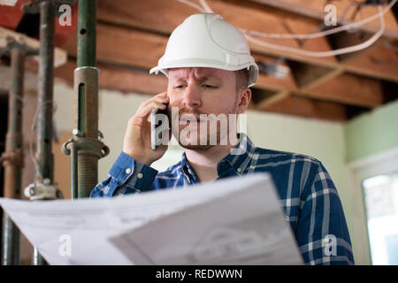 Architect Inside House Being Renovated Studying Plans Talking On Mobile Phone Stock Photo