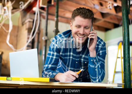 Architect Inside House Being Renovated Working On Plans Using Laptop And Talking On Cellphone Stock Photo